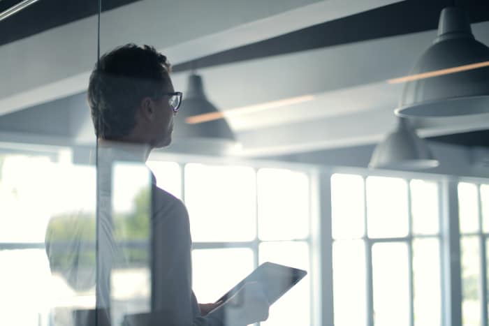 a digital marketing manager presenting behind a glass panel, holding a digital tablet to enhance his presentation.